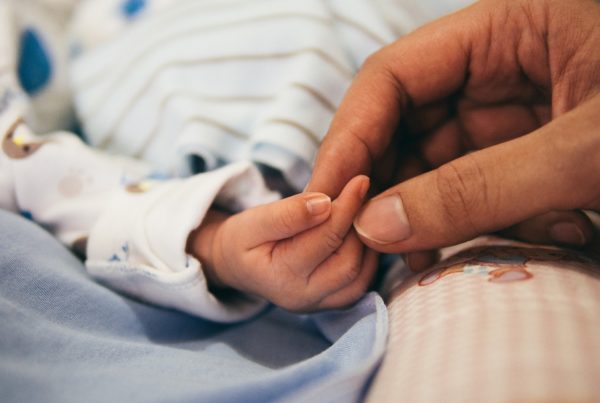 An adult hand caresses the fingers of a newborn baby.