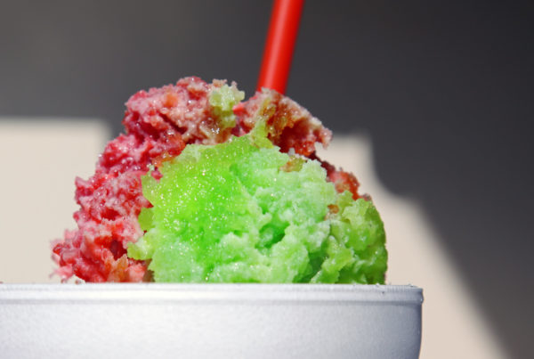 a close-up photo of the crown of a green and red snow cone in a styrofoam cup with a red straw