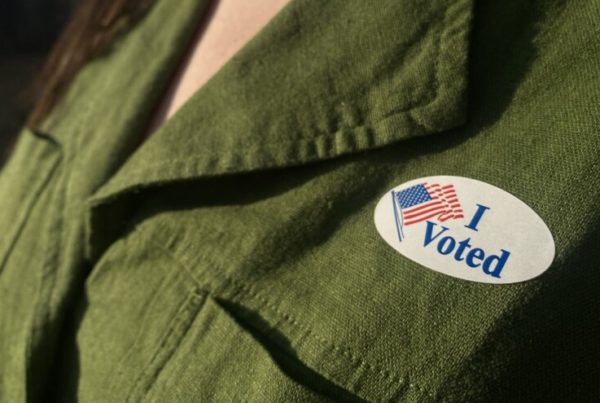 A close-up photo of an "I Voted" sticker on a person wearing a dark green dress shirt.