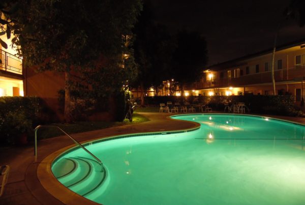 a kidney-shaped pool int he middle of an apartment complex glows with green light at night