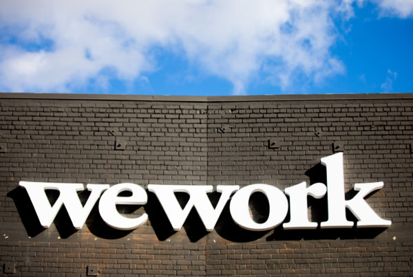 A white WeWork logo on black brick with a blue sky overhead.