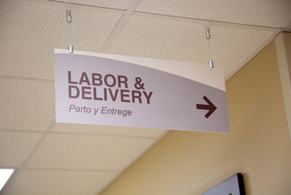 A sign hanging from the ceiling of a hallway points people to the labor and delivery area of a hospital.