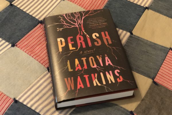 a photo of the hardcover book "Perish" by LaToya Watkins. The book is lying on a colorful quilt. The book cover includes an image of a tree with sprawling branches and roots.