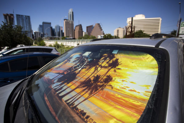 A sun shade depicting a sunset on a car parked at Vic Mathias Shores and the Austin city skyline on a hot day.