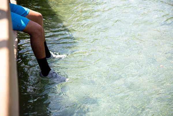 A runner dipping his shoes in the San Marcos River to cool off after running in the summer heat.