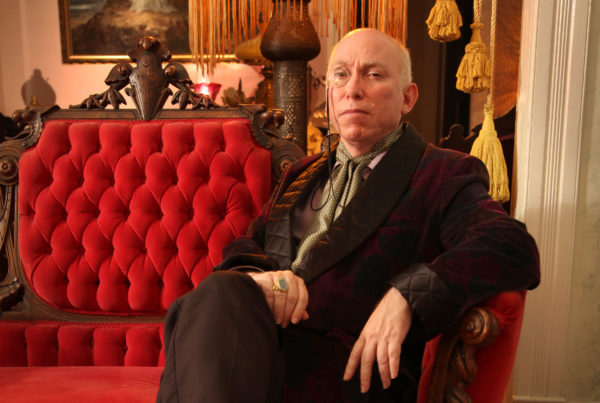 A man sits on red cushioned antique chair.