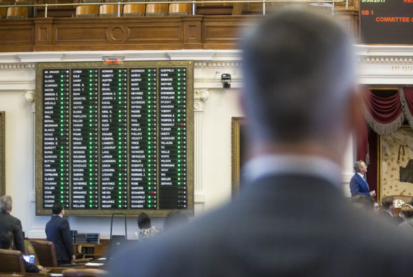 Voting during a session of the Texas House of Representatives. The back of a man's head is in the foreground, while a sign with legislators' names and votes is in the background. Gabriel Cristóver Pérez/KUT News.