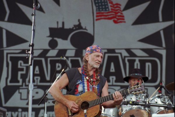 Willie Nelson sings on stage with his guitar, Trigger, in his arms.