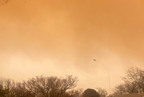 A reddish-brown dust clouds are seen over treetops and roofs in a Lubbock neighborhood, rendering the whole image in a sepia tone.