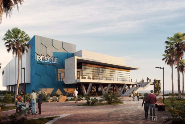A CGI rendering of the new Port of Corpus Christi Wildlife Rescue Center is seen. The building is blue and white and appears to be two stories tall with a staircase leading up to the second floor. Large, glass windows look out over a balcony area. The building is surrounded by palm trees and the gulf waters can be seen in the distance.