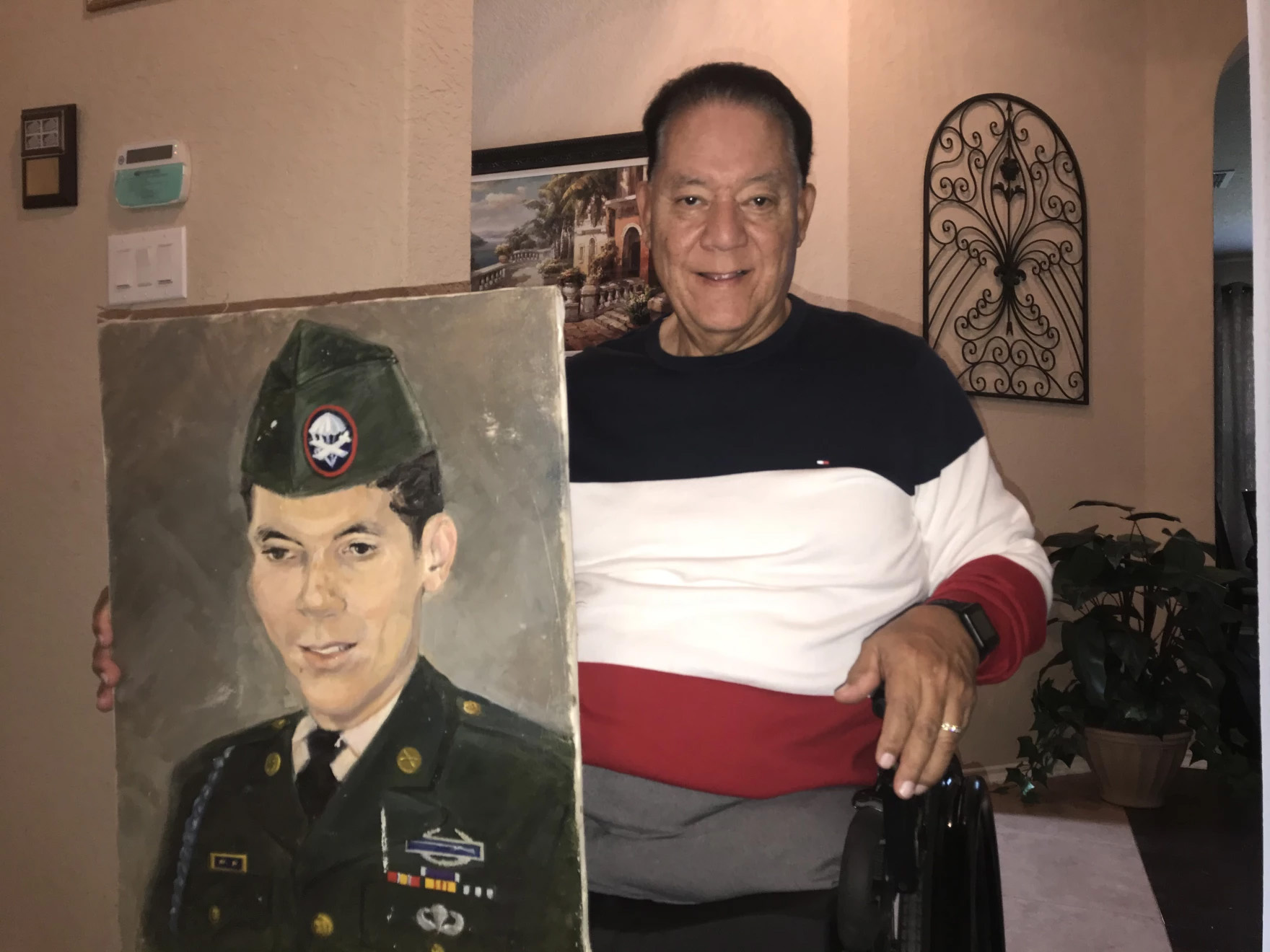 A man faces the camera holding a painting showing the portrait of a military serviceman.