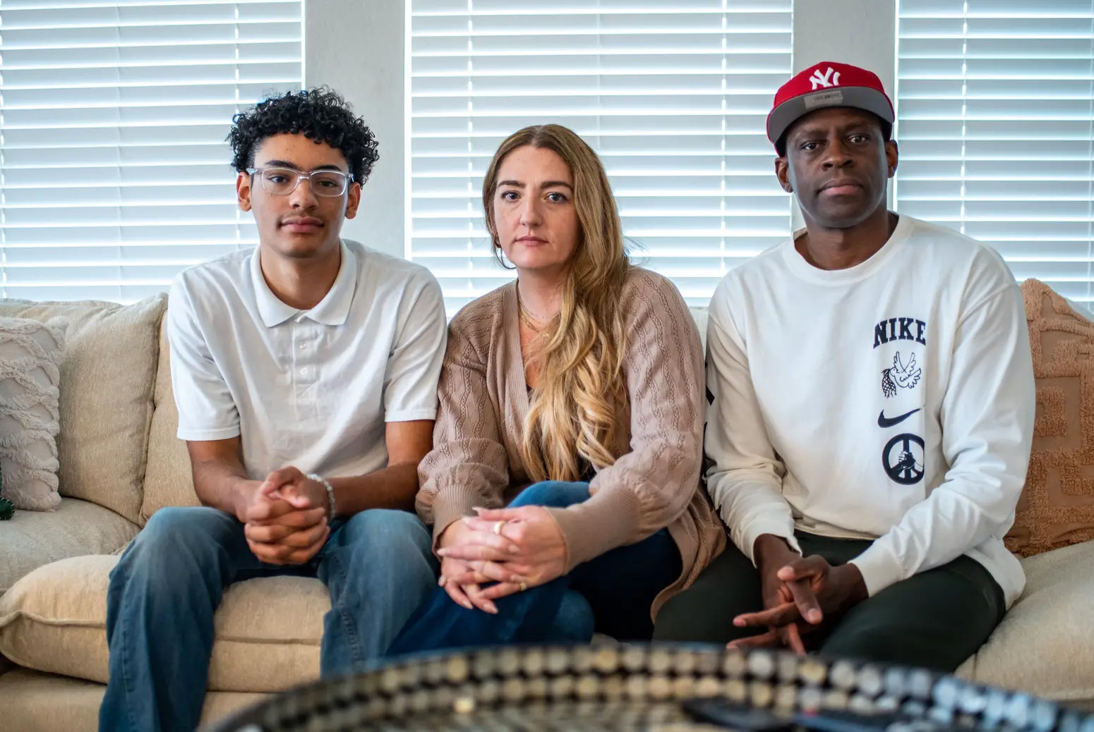 Three people are seen seated on a couch facing towards the camera. From left to right is teen Myles Leon and his mother Amy and father Oveimar.