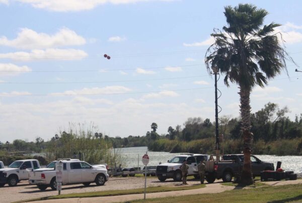 A mobile surveillance camera vehicle is seen alongside several Border Patrol trucks next to a boat launch.