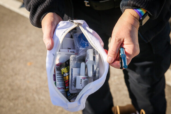 Hands holding a packet of narcan nasal sprays and other medications