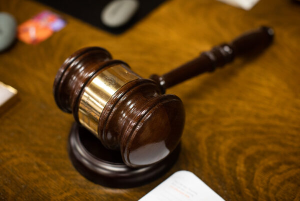 A close-up shot of a wooden gavel with a gold band down the middle, on a wooden table