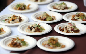 Rows of paper plates, each with open taco containing meat, cheese and cilantro