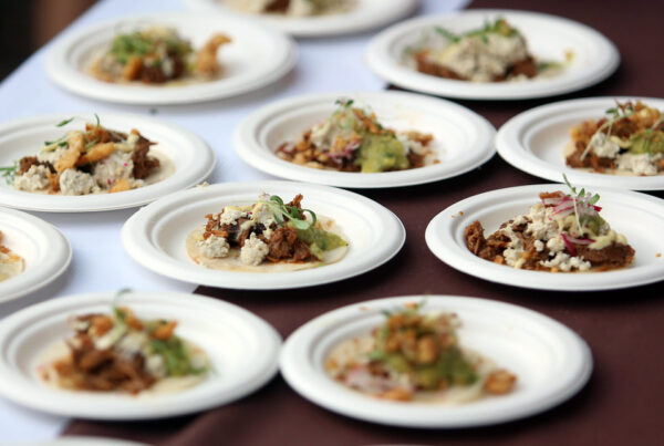 Rows of paper plates, each with open taco containing meat, cheese and cilantro