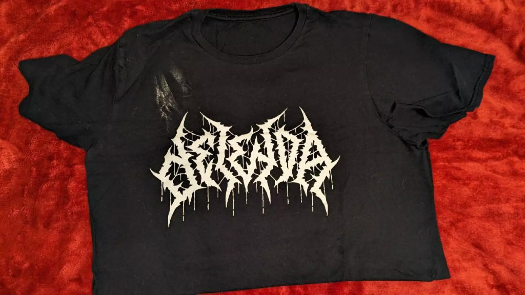A black t-shirt with the name of the band Delenda written in a spiky black metal font is seen.