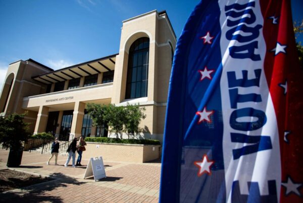 A red, white and blue banner that says "Vote Aqui" is seen in front of The Texas State performing arts building