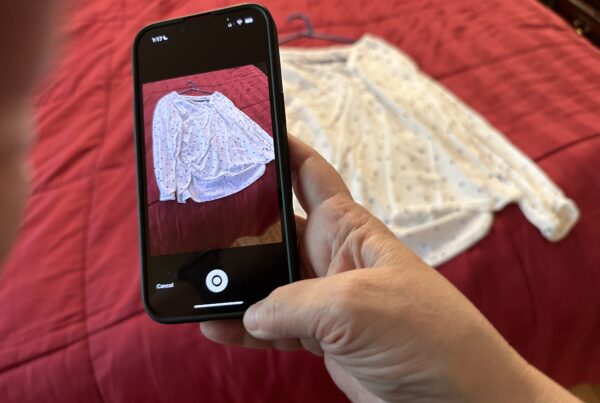 A photo of a smartphone taking a picture of a shirt resting on a bed.