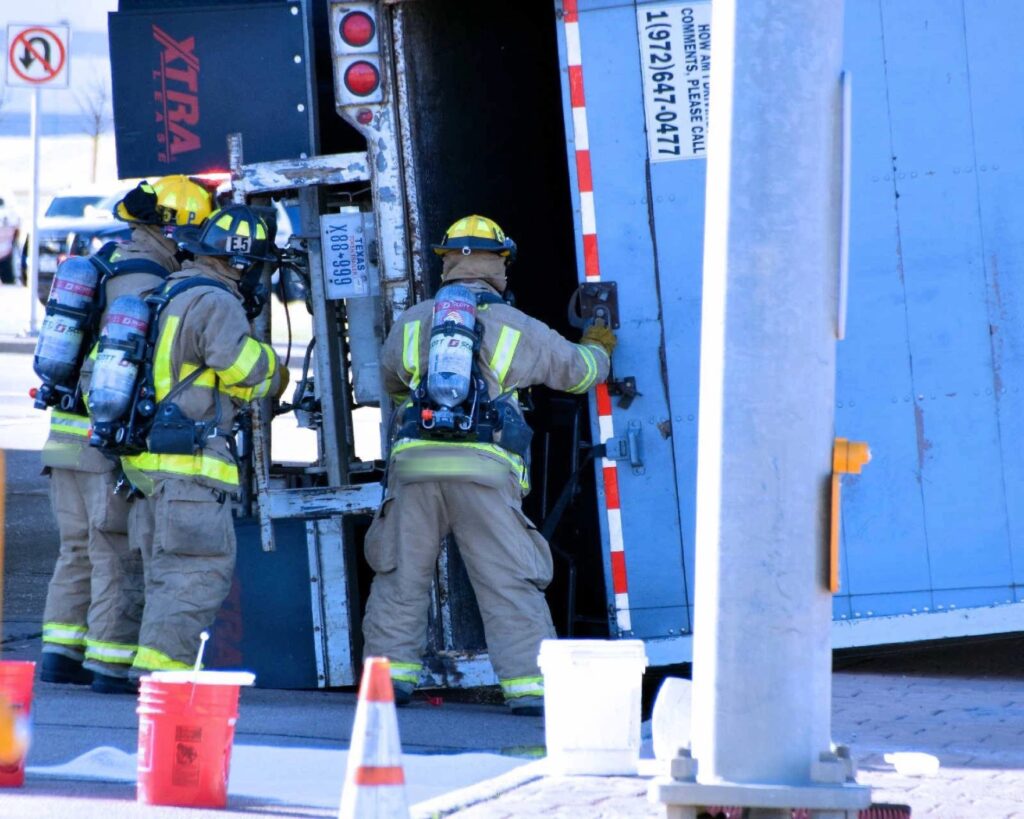 firefighters in full gear approach an overturned truck