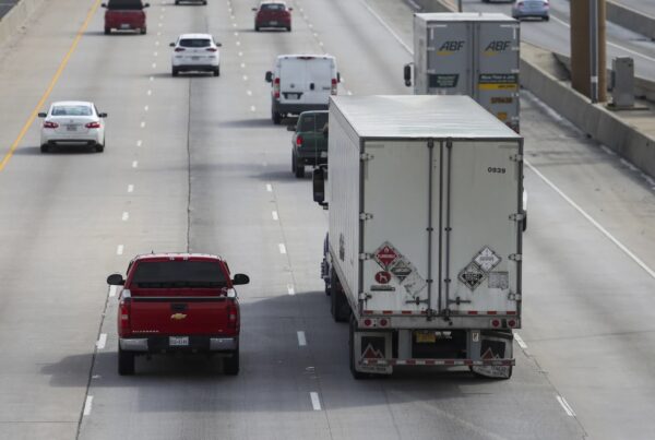 passenger vehicles share a four lane highway with a semi truck with signs warning it is carrying hazardous materials