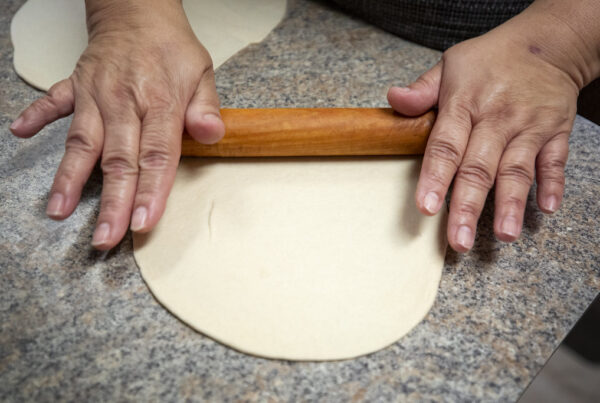 a close-up photo of hands rolling a tortilla on a stone surface
