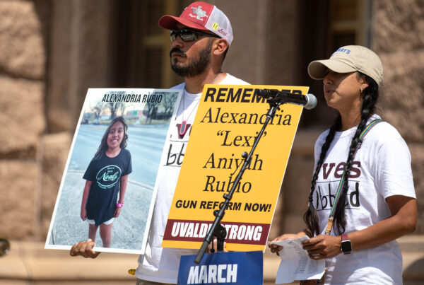 Two people hold signs honor Lexi Rubio as they speak into a microphone outside of the Texas Capitol building.