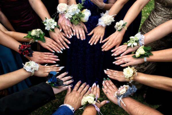 a photo of a bunch of people with different painted nails and wrist corsages putting their hands into a circle