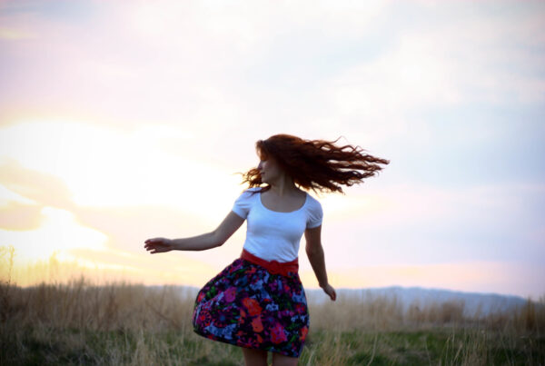 a woman spins in an open field as the sun begins to set
