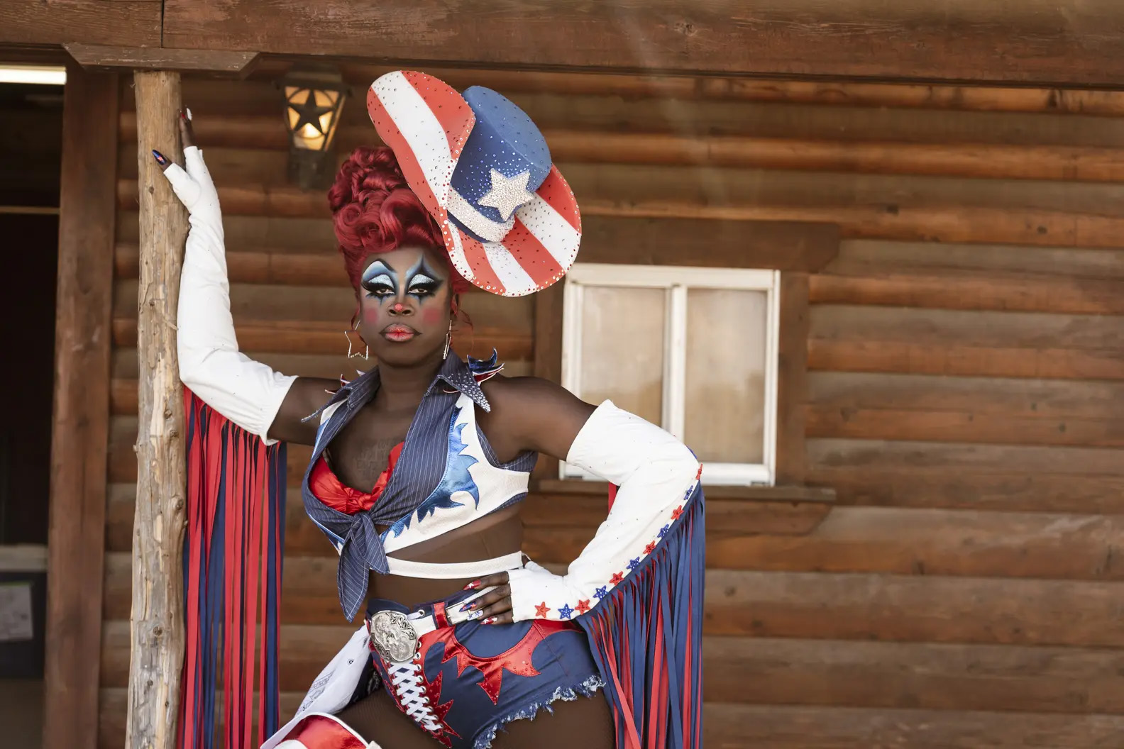 A person dressed in drag strikes a pose. He's wearing a western-themed red, white and blue outfit and heavy makeup. This is Bob, a drag queen.
