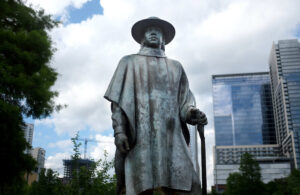 A photo of the Stevie Ray Vaughan statue near Lady Bird Lake in Austin. A part of the Austin skyline is visible behind it.