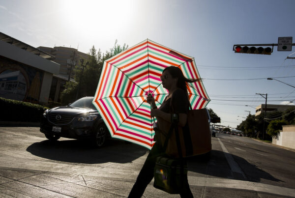 The silhouette of a woman against the backdrop of her colorful, striped umbrella which she is using to block the sun.