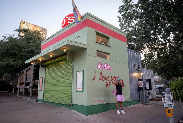 A man wearing pink shorts stands in front of a Barbie mural at Jo's Coffee on South Congress.