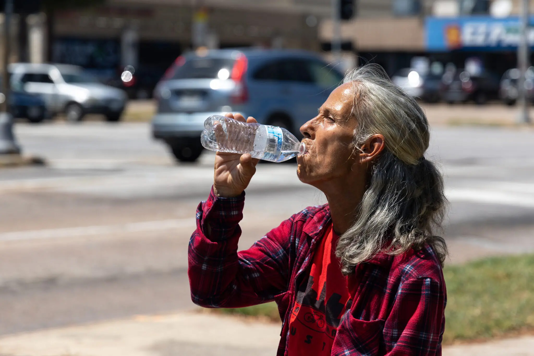 A grey-haired woman takes a drink from a bottle of water on a sunny day outside.