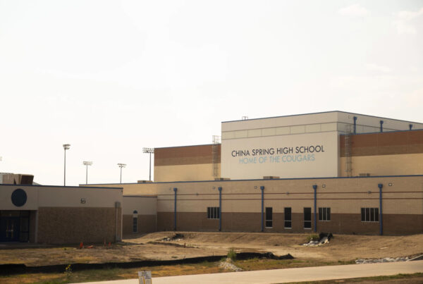 The outside of a high school campus is seen. The main building bears the words "China Spring High School, Home of the Cougars."