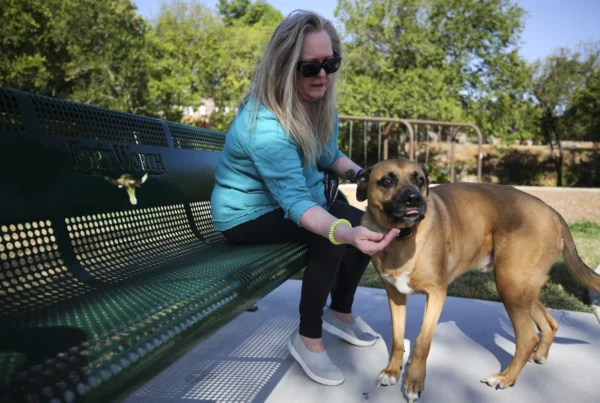 A woman sits on a bench, petting a large dog.