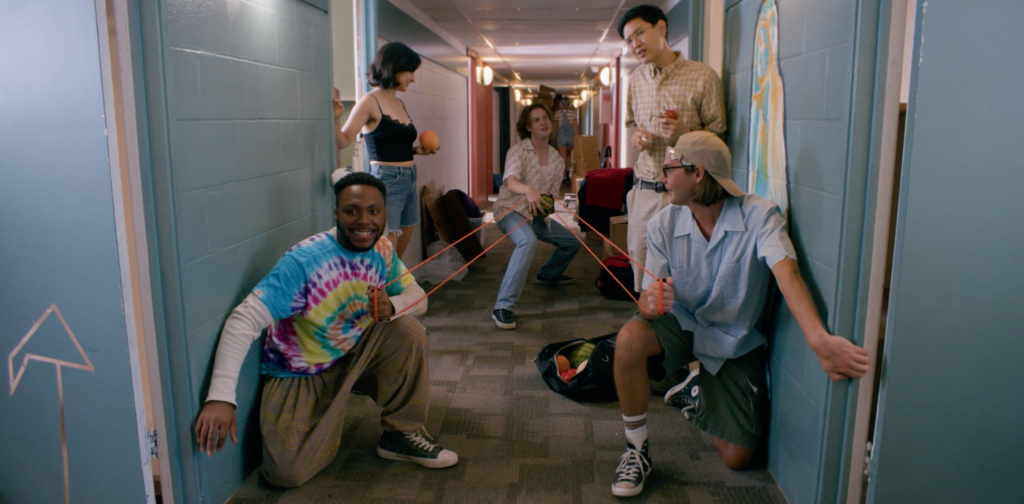 A group of young actors gather in a hallway and play with an extra large slingshot.