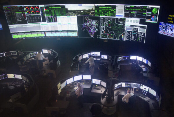 An overhead photograph shows several people looking at computer monitors and a big wall of maps and grids.