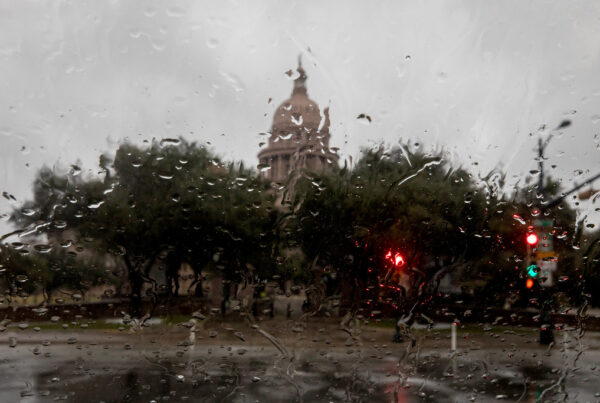 The view from inside a car of a rainy windshield with the Texas Capitol building in the distance