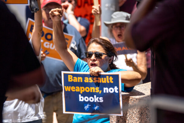 A woman raises a fist and chants while holding a sign reading "Ban assault weapons, not books" during a rally.