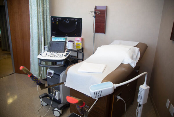 A clinic room with a patient table and ultrasound machine