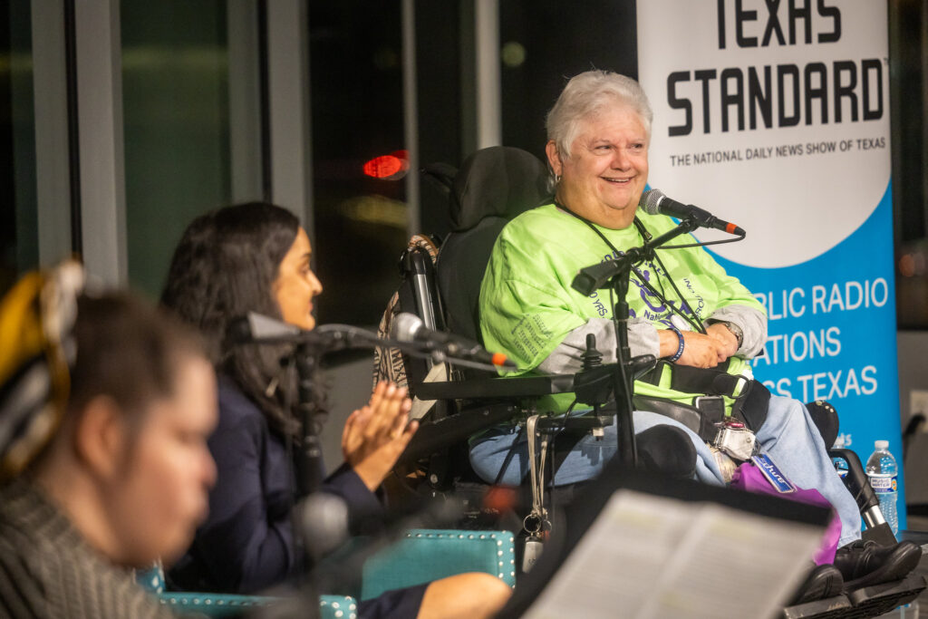 A photo shows the three panelists with Nancy Crowther in focus. She has short silver hair and is wearing a bright green t-shirt. She smiles while at the microphone.