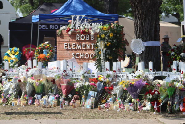 White crosses bearing the names of those killed in the Robb Elementary school shooting are surrounded by numerous bouquets, small U.S. flags, wreaths and candles outside of the school itself.