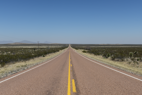A view of an empty two-lane highway with blue sky on the horizon