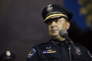 A close-up photo of Art Acevedo in full police uniform and hat standing at a microphone for an event.