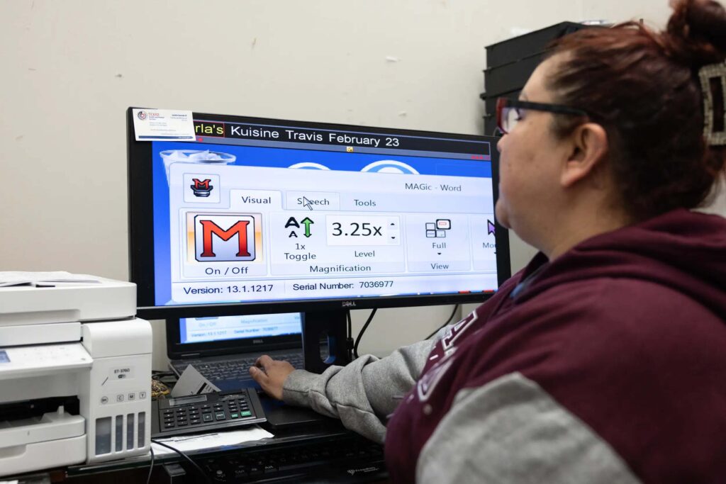 A woman sits at a desk looking at a computer monitor that displays enlarged software for low-vision users