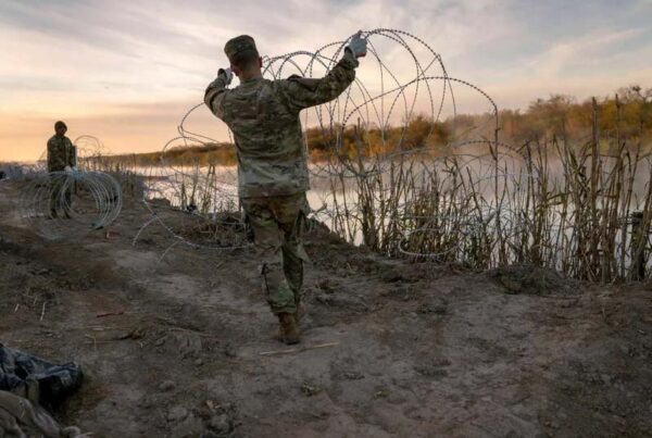 A uniformed Texas National Guard soldier holds up concertina wire as he works to install it along the banks of the Rio Grande.