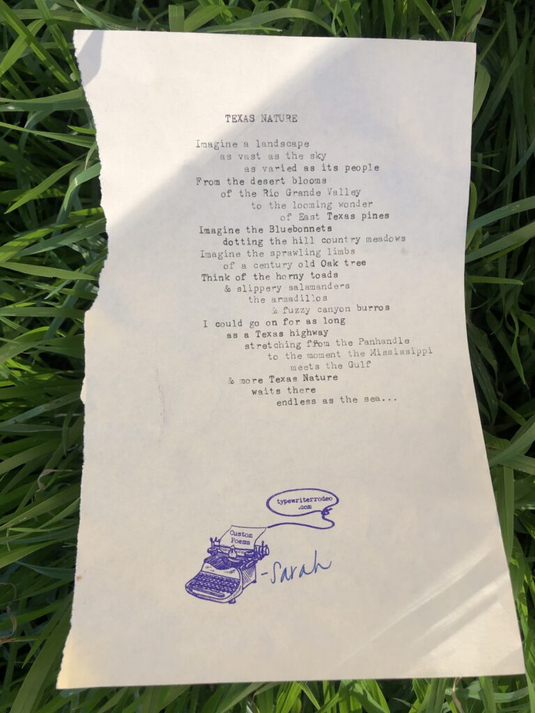 A photo of the typewritten poem on a torn half sheet of light yellow paper. The paper is resting on a bed of green grass.