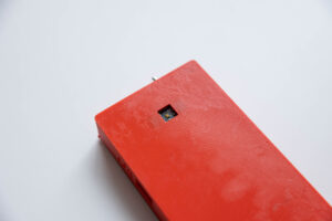A rectangular LightSound device that is red in color and has a tiny square cut out near its top edge